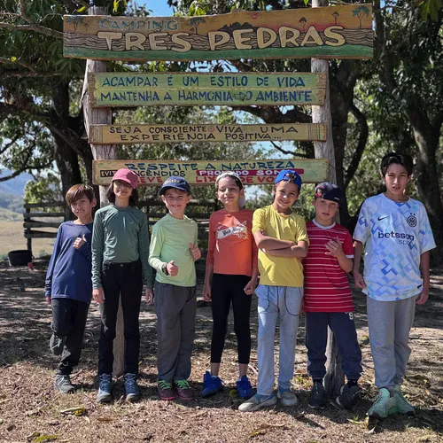Grupo de crianças posando em frente à placa do Camping Três Pedras durante o acampamento